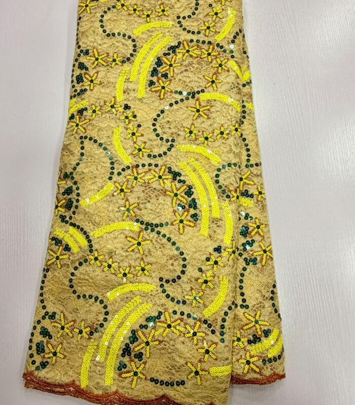 Elevate your occasion wear with this premium gold net lace fabric, meticulously detailed with vibrant yellow sequential embroidery and deep green accent sequins. Designed on a durable mesh base, this fabric features dynamic geometric swoops and star-burst floral motifs that catch the light from every angle. The scalloped copper-toned border adds a refined finishing edge to hems and sleeves.